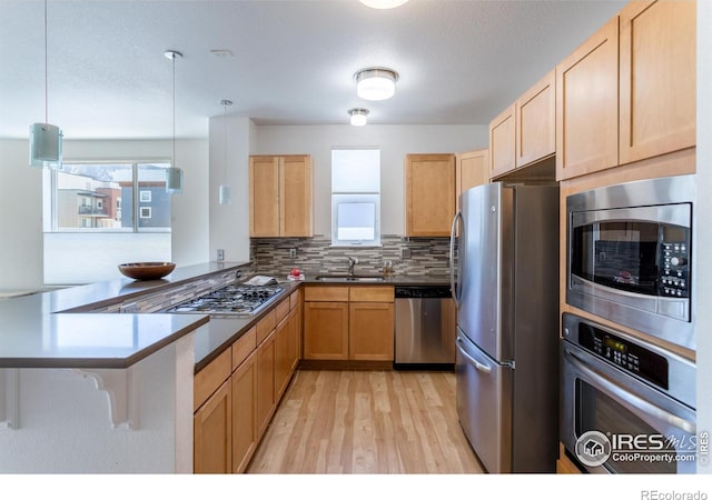 kitchen with sink, pendant lighting, appliances with stainless steel finishes, and kitchen peninsula