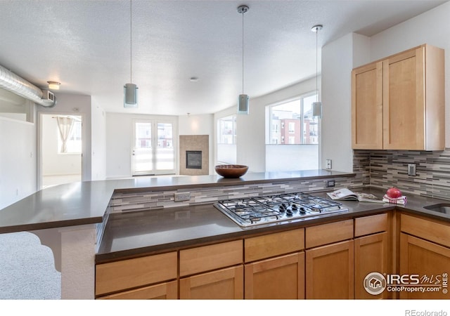 kitchen featuring kitchen peninsula, decorative backsplash, stainless steel gas cooktop, hanging light fixtures, and a textured ceiling