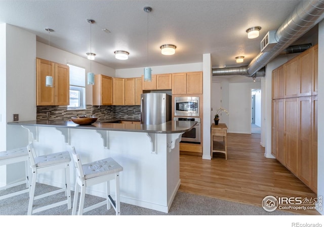 kitchen with kitchen peninsula, stainless steel appliances, backsplash, pendant lighting, and a breakfast bar