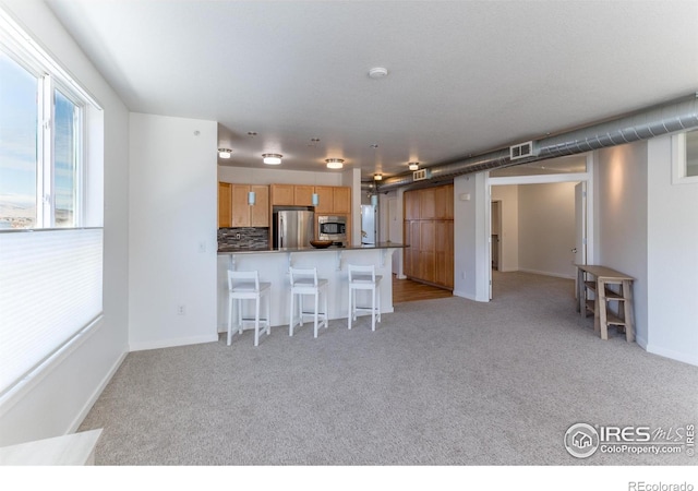 kitchen with light colored carpet, stainless steel appliances, a breakfast bar area, and tasteful backsplash