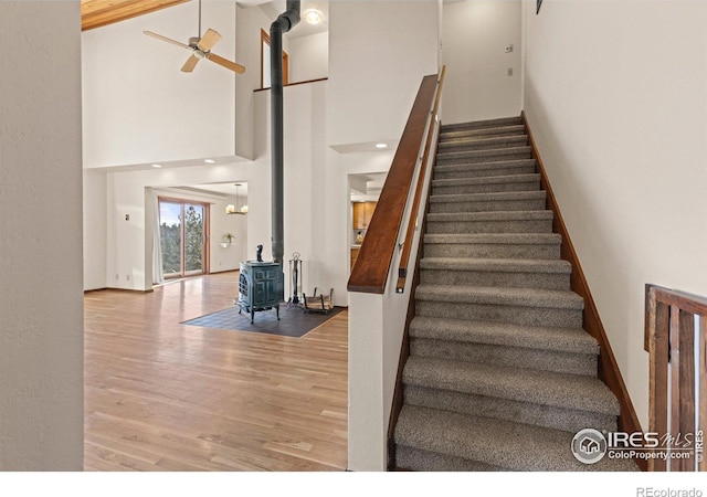 stairway featuring ceiling fan, a towering ceiling, a wood stove, and hardwood / wood-style floors