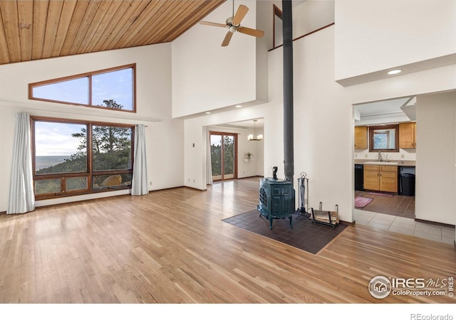 unfurnished living room featuring sink, light wood-type flooring, wood ceiling, a wood stove, and high vaulted ceiling