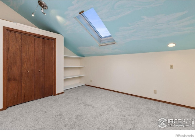 additional living space with vaulted ceiling with skylight, built in shelves, and light carpet