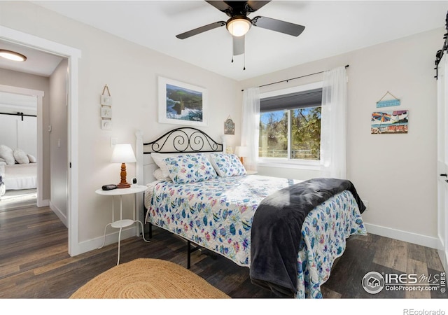 bedroom featuring dark wood-type flooring, ceiling fan, and a barn door