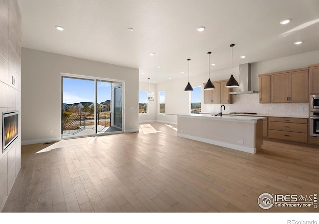 kitchen with light hardwood / wood-style floors, pendant lighting, sink, a kitchen island with sink, and wall chimney exhaust hood