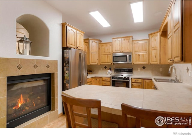 kitchen with kitchen peninsula, stainless steel appliances, decorative backsplash, tile counters, and sink