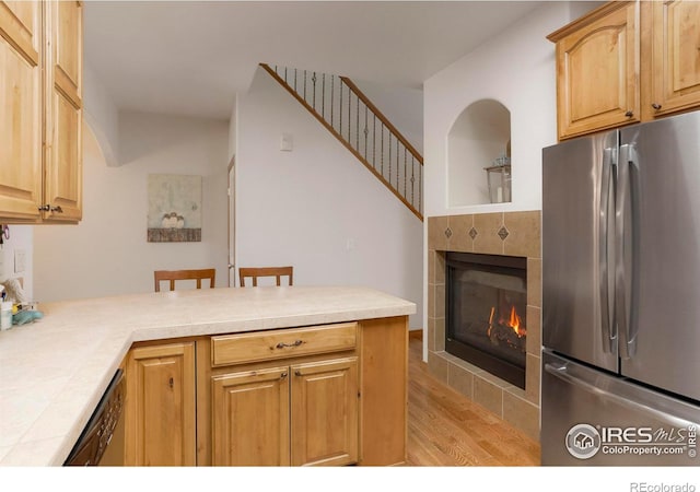 kitchen featuring kitchen peninsula, stainless steel fridge, a breakfast bar area, a tiled fireplace, and light hardwood / wood-style flooring