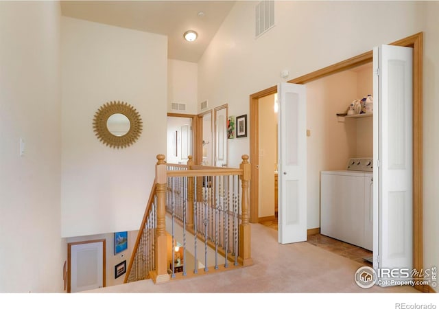 corridor with high vaulted ceiling, washer / clothes dryer, and light colored carpet