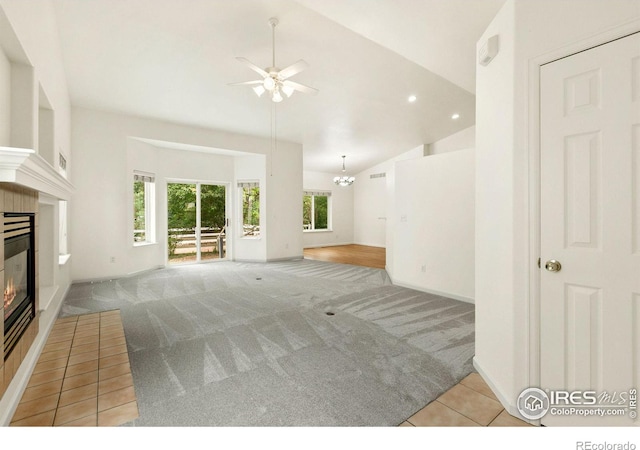 unfurnished living room featuring ceiling fan with notable chandelier, light colored carpet, a wealth of natural light, and lofted ceiling