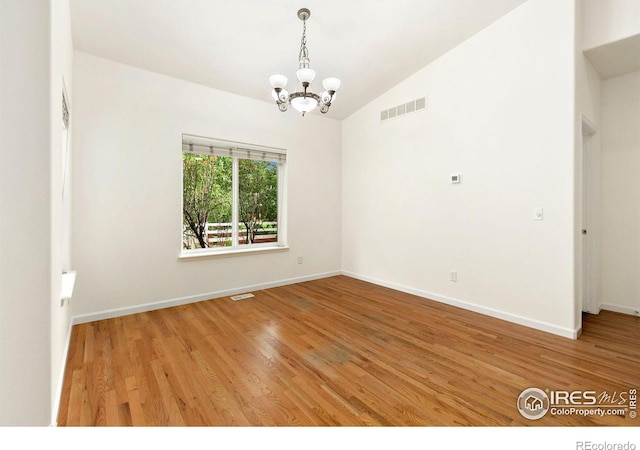 spare room featuring hardwood / wood-style floors, lofted ceiling, and an inviting chandelier