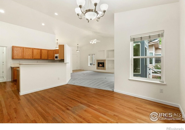 unfurnished living room featuring lofted ceiling, ceiling fan with notable chandelier, and light hardwood / wood-style flooring