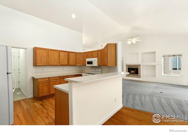 kitchen with kitchen peninsula, ceiling fan, white appliances, light wood-type flooring, and high vaulted ceiling