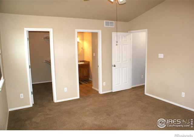 unfurnished bedroom featuring dark colored carpet, ensuite bath, a closet, vaulted ceiling, and a walk in closet