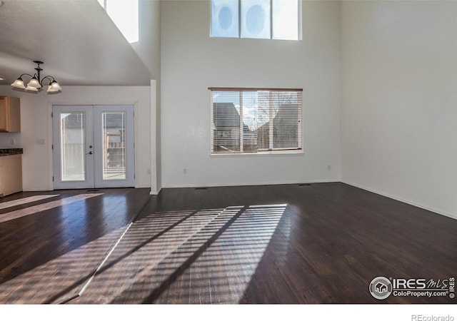 unfurnished living room with a high ceiling, a chandelier, dark hardwood / wood-style flooring, and french doors