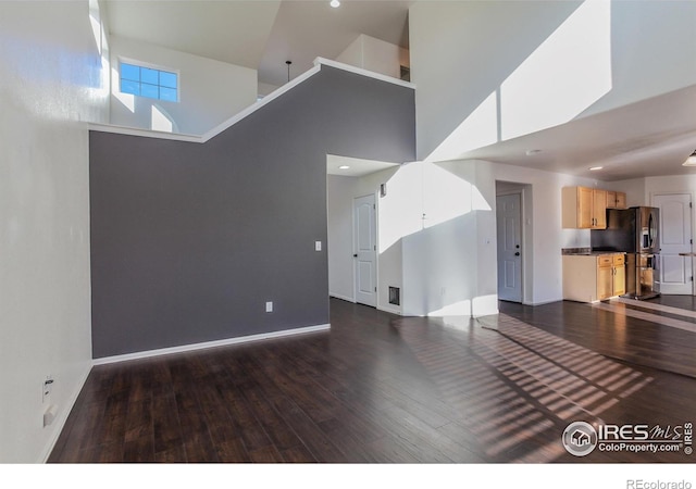 unfurnished living room with dark wood-type flooring and a towering ceiling