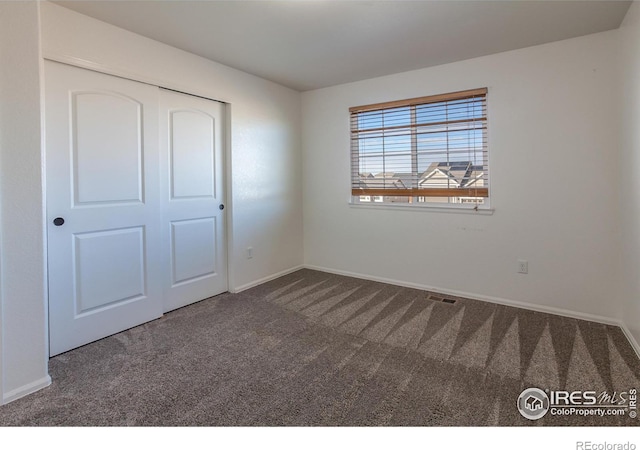 unfurnished bedroom with dark carpet and a closet