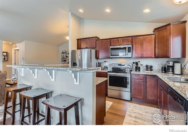 kitchen featuring a kitchen island, appliances with stainless steel finishes, lofted ceiling, sink, and light hardwood / wood-style flooring