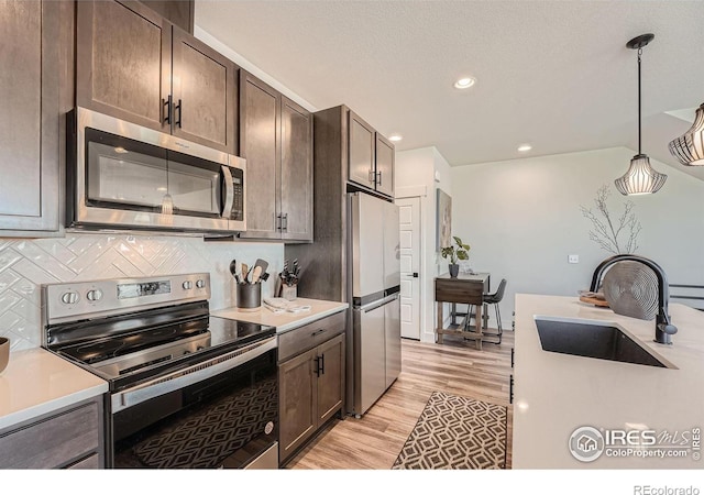 kitchen with sink, backsplash, hanging light fixtures, dark brown cabinetry, and stainless steel appliances