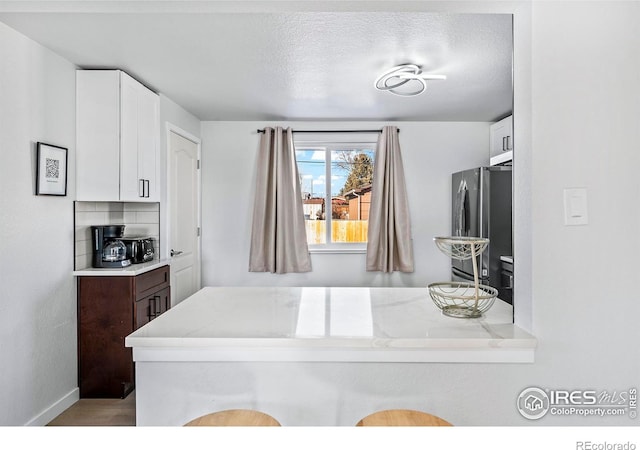 kitchen featuring kitchen peninsula, stainless steel fridge, and white cabinetry