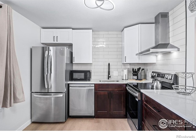 kitchen with white cabinetry, stainless steel appliances, dark brown cabinets, wall chimney range hood, and sink