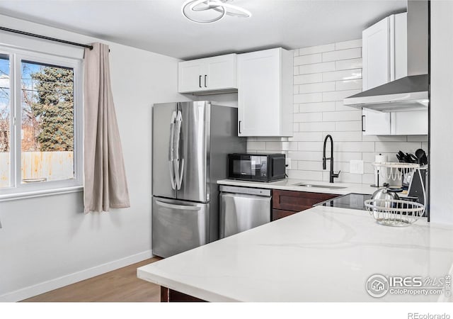 kitchen featuring light stone countertops, wall chimney range hood, stainless steel appliances, decorative backsplash, and sink