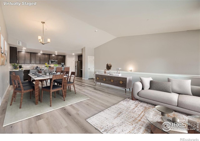 living room with vaulted ceiling, an inviting chandelier, and light hardwood / wood-style flooring