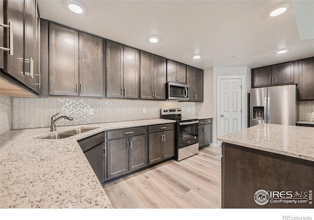 kitchen with appliances with stainless steel finishes, light hardwood / wood-style floors, dark brown cabinets, and light stone countertops