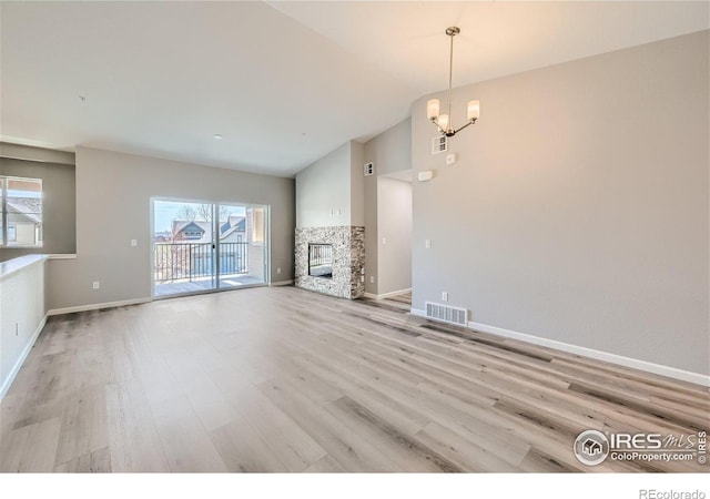 unfurnished living room with vaulted ceiling, an inviting chandelier, a fireplace, and light wood-type flooring