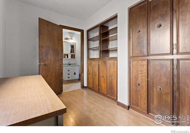 interior space featuring a textured ceiling, built in features, and light hardwood / wood-style flooring