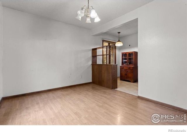 empty room with a textured ceiling, an inviting chandelier, and light hardwood / wood-style flooring