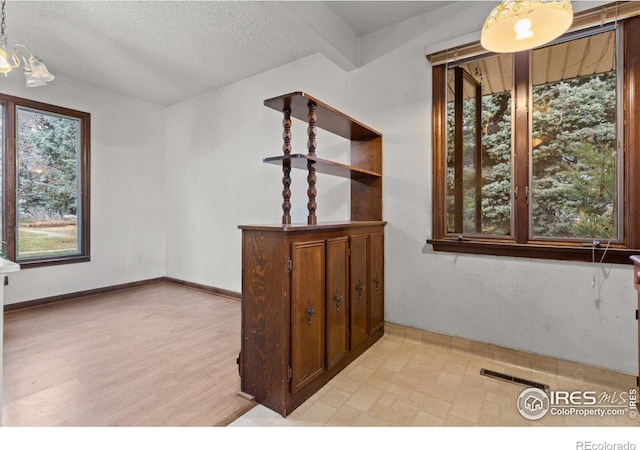 interior space with beamed ceiling, a textured ceiling, and light hardwood / wood-style flooring