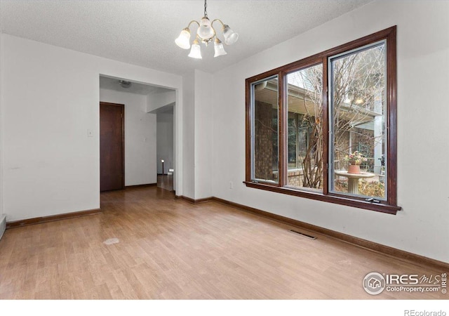 empty room featuring a notable chandelier, a textured ceiling, and light hardwood / wood-style flooring