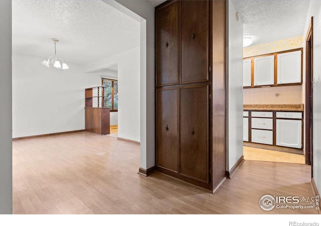 corridor featuring a textured ceiling, a chandelier, and light wood-type flooring