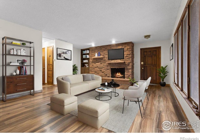 living room featuring built in features, a stone fireplace, a textured ceiling, and hardwood / wood-style floors