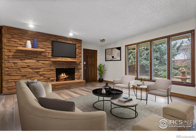 living room featuring wood-type flooring, a stone fireplace, and a textured ceiling