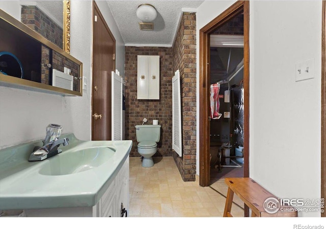 bathroom featuring toilet, brick wall, a textured ceiling, ornamental molding, and vanity