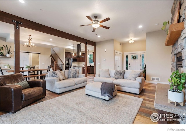 living room featuring ceiling fan with notable chandelier, hardwood / wood-style floors, beam ceiling, and a fireplace