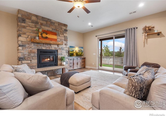 living room featuring a stone fireplace, light wood-type flooring, and ceiling fan