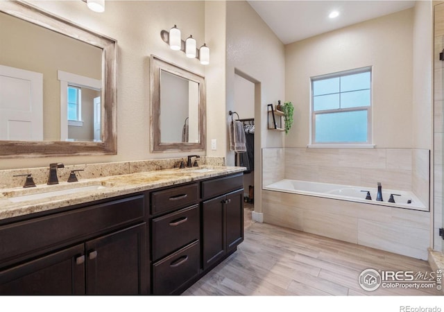 bathroom featuring tiled bath, hardwood / wood-style floors, and vanity