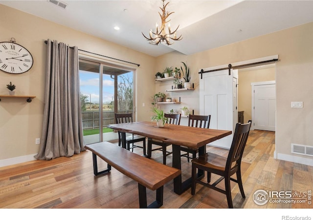 dining room with a barn door, a notable chandelier, and light wood-type flooring