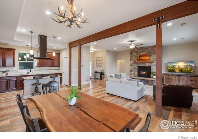 dining room featuring a fireplace, sink, light wood-type flooring, a barn door, and ceiling fan with notable chandelier