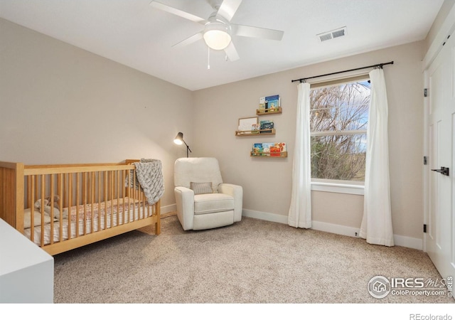 carpeted bedroom featuring ceiling fan and a crib