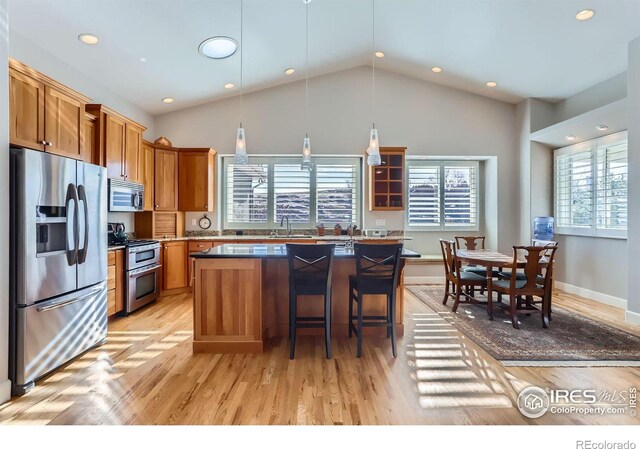 kitchen with a breakfast bar, appliances with stainless steel finishes, a kitchen island, decorative light fixtures, and light wood-type flooring