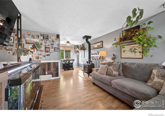 living room featuring ceiling fan, light hardwood / wood-style floors, a textured ceiling, and a wood stove