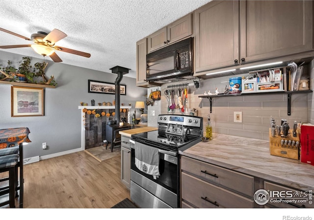 kitchen with stainless steel electric stove, wood counters, a wood stove, decorative backsplash, and light wood-type flooring