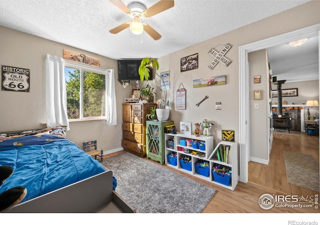 bedroom with hardwood / wood-style flooring, ceiling fan, a textured ceiling, and a wood stove