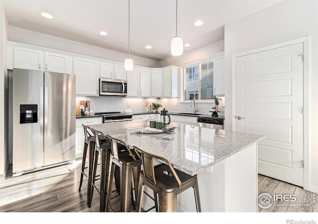 kitchen featuring decorative light fixtures, tasteful backsplash, a kitchen island, white cabinetry, and stainless steel appliances