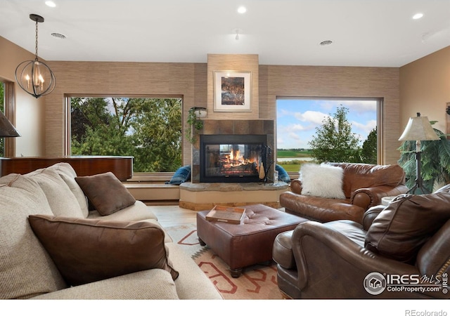 living room featuring light hardwood / wood-style flooring, an inviting chandelier, a tiled fireplace, and a healthy amount of sunlight