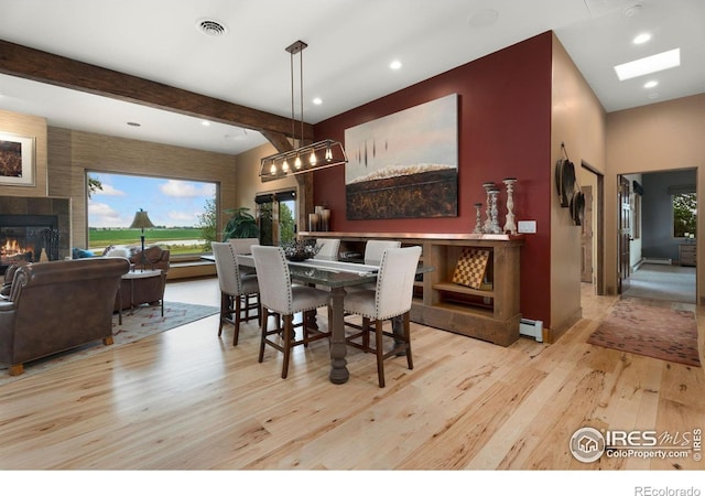 dining space with light wood-type flooring, a baseboard heating unit, a fireplace, and beamed ceiling