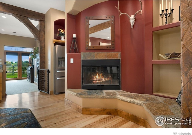 living room with built in shelves, a stone fireplace, and light wood-type flooring